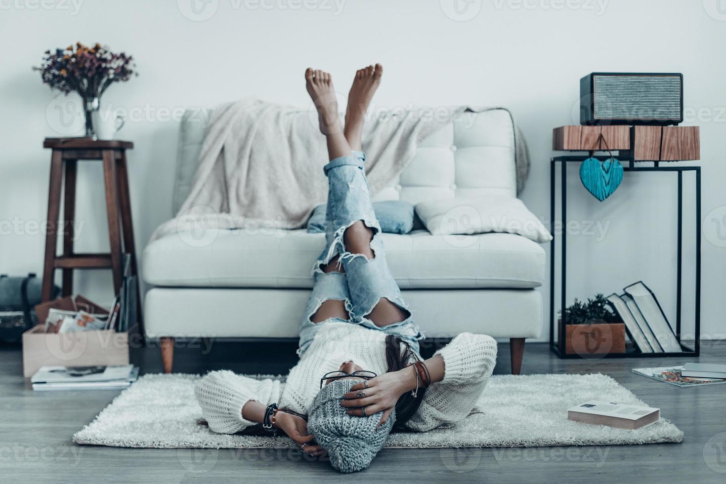 passar o tempo despreocupado. mulher jovem e bonita com roupa casual, tocando a cabeça com a mão enquanto estava deitado no chão em casa foto