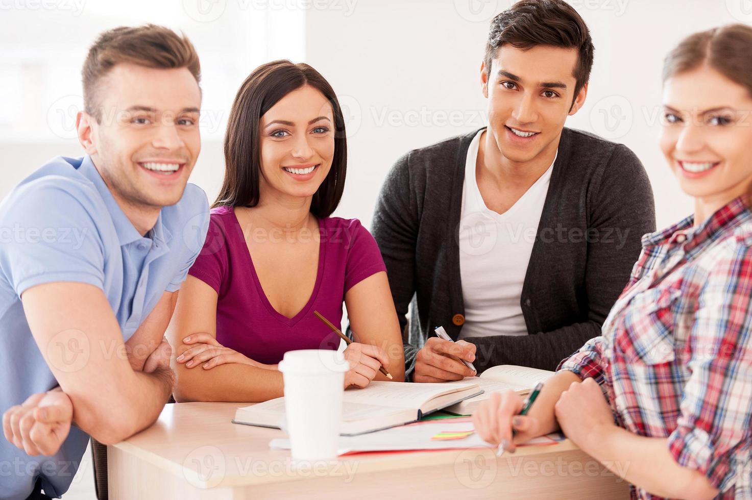 alunos estudando juntos. quatro estudantes alegres estudando sentados à mesa juntos e sorrindo para a câmera foto