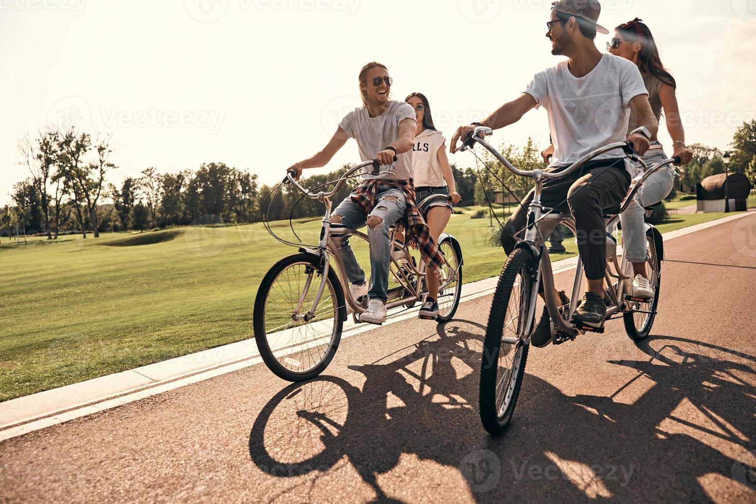 melhor dia de todos. grupo de jovens felizes em roupas casuais sorrindo enquanto andam de bicicleta juntos ao ar livre foto