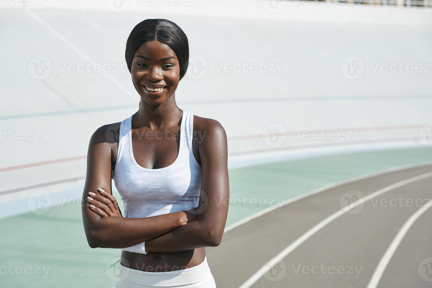 bela jovem africana em roupas esportivas, mantendo os braços cruzados e sorrindo em pé ao ar livre foto