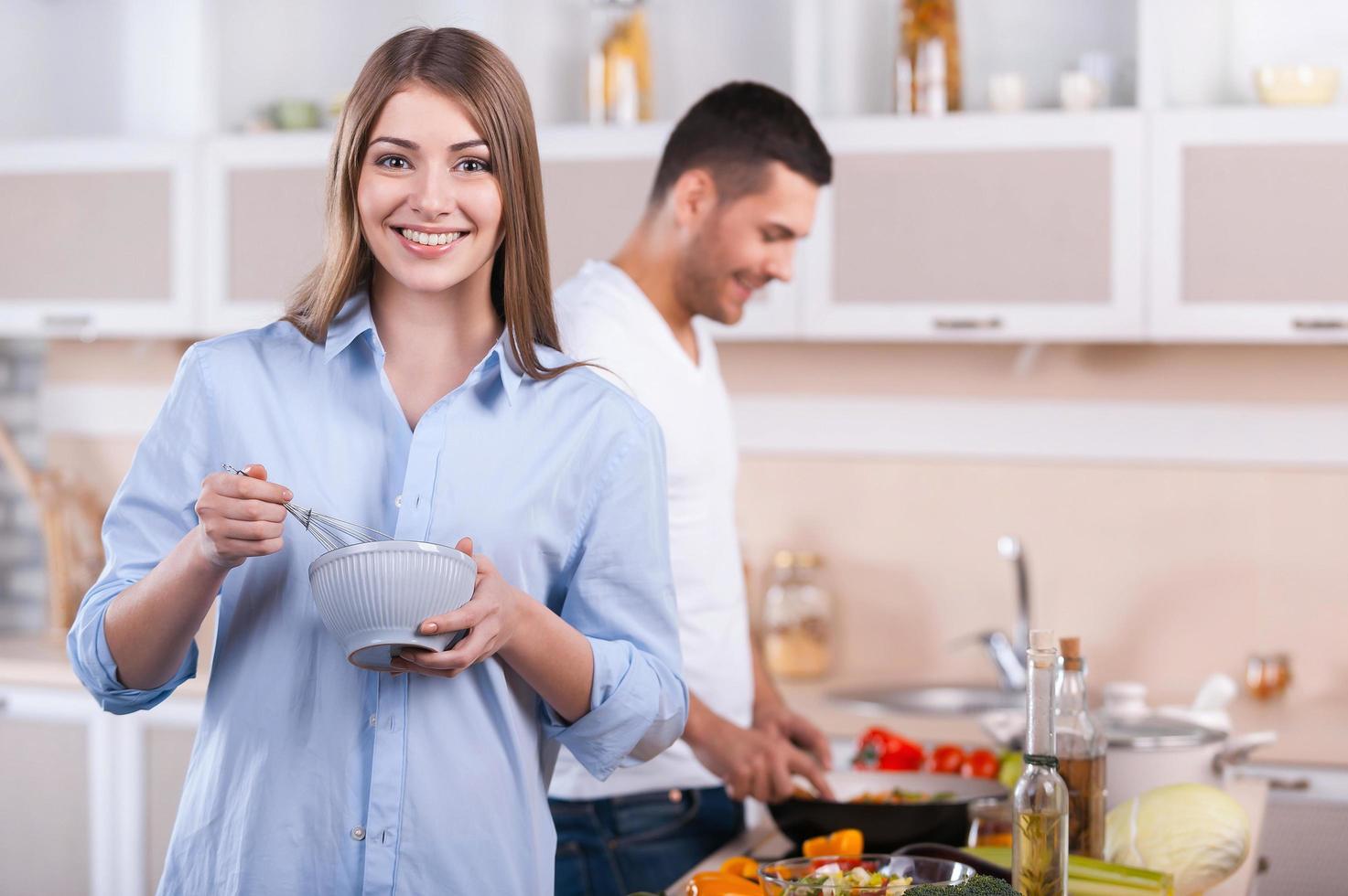 cozinhando o café da manhã juntos. casal feliz cozinhando juntos na cozinha enquanto mulher olhando para a câmera e sorrindo foto