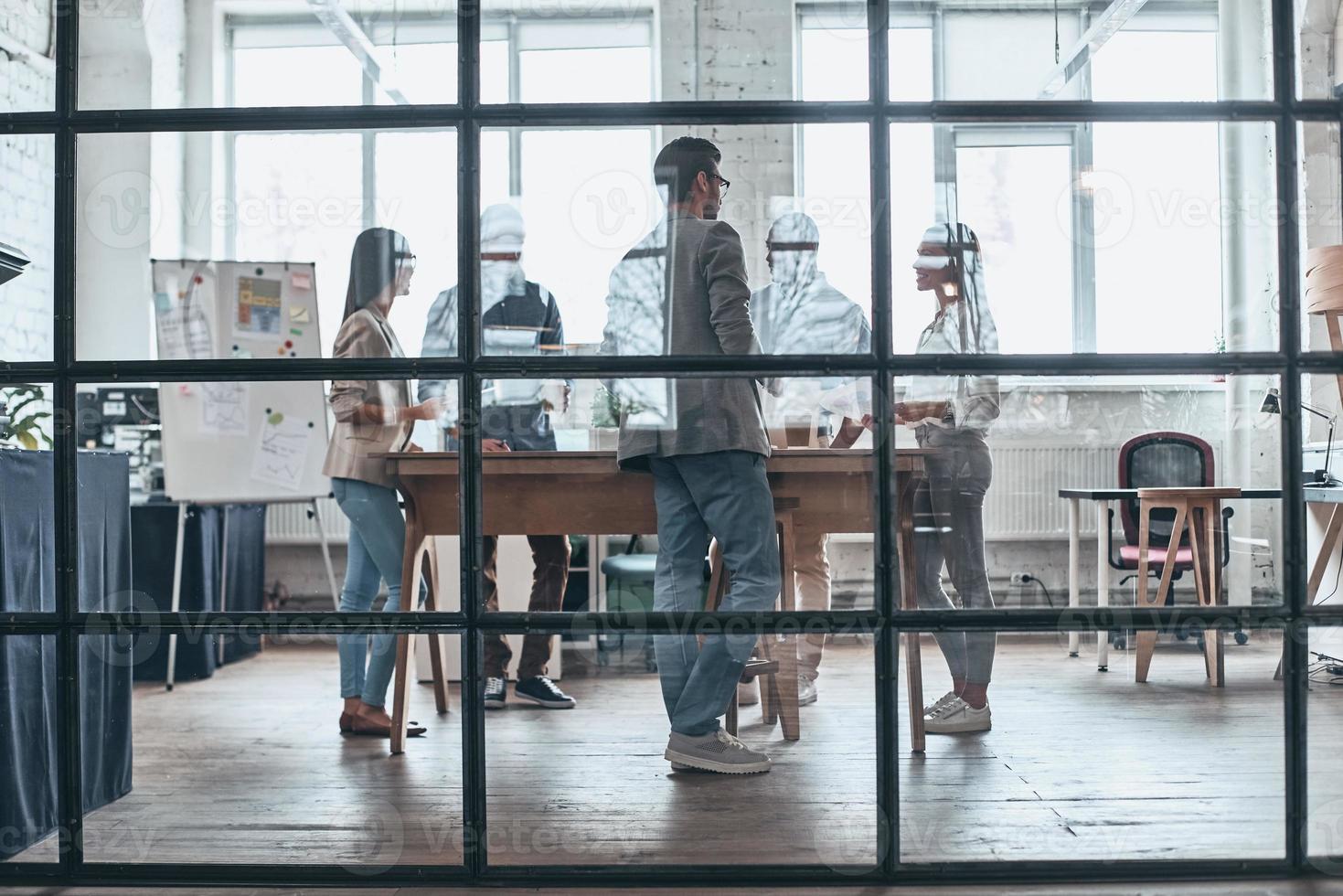 dia de trabalho ocupado. comprimento total de jovens modernos trabalhando e se comunicando juntos enquanto estão atrás da parede de vidro na sala de reuniões foto