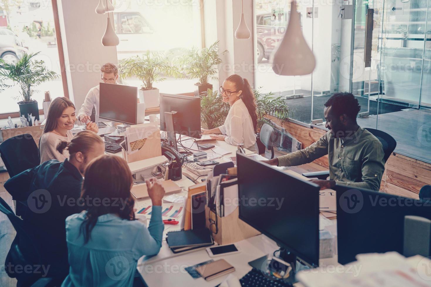 grupo de jovens modernos em roupas casuais inteligentes se comunicando e usando tecnologias modernas enquanto trabalhava no escritório foto