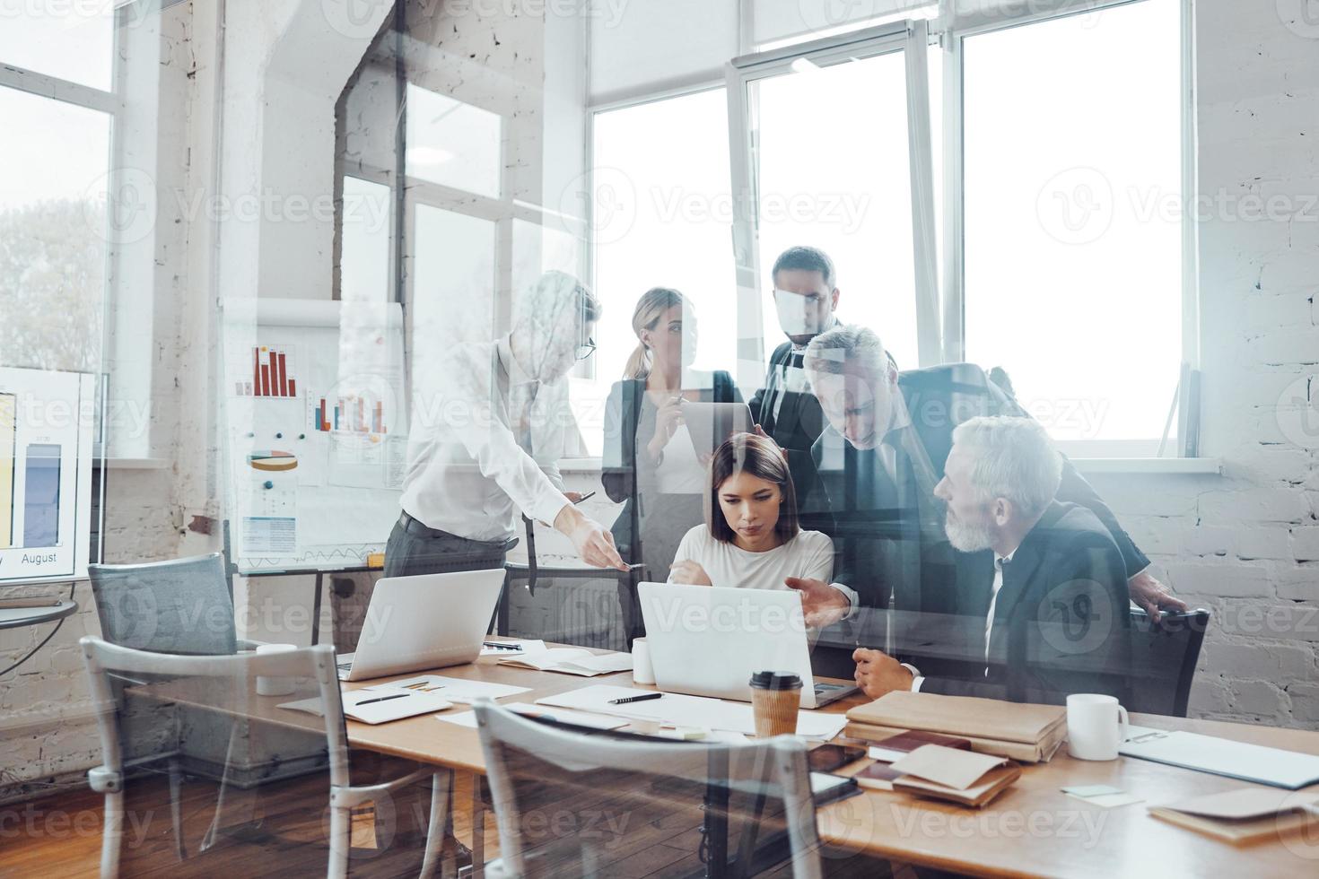 equipe de negócios automotivada analisando as vendas usando tecnologias modernas enquanto a equipe se reúne na sala de reuniões foto