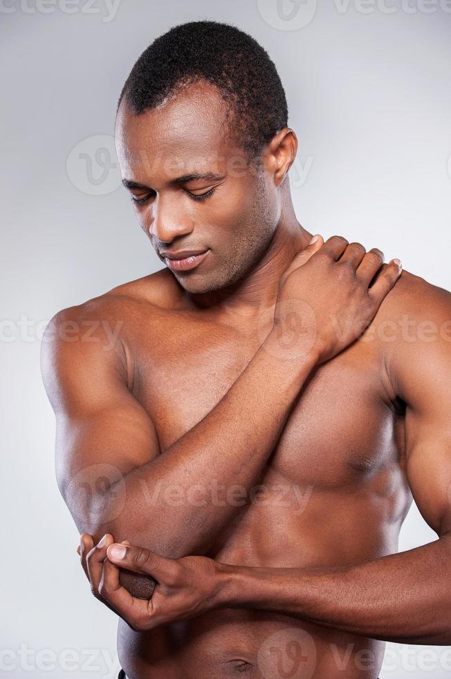 sentindo dor no cotovelo. jovem africano musculoso tocando seu cotovelo em pé contra um fundo cinza foto