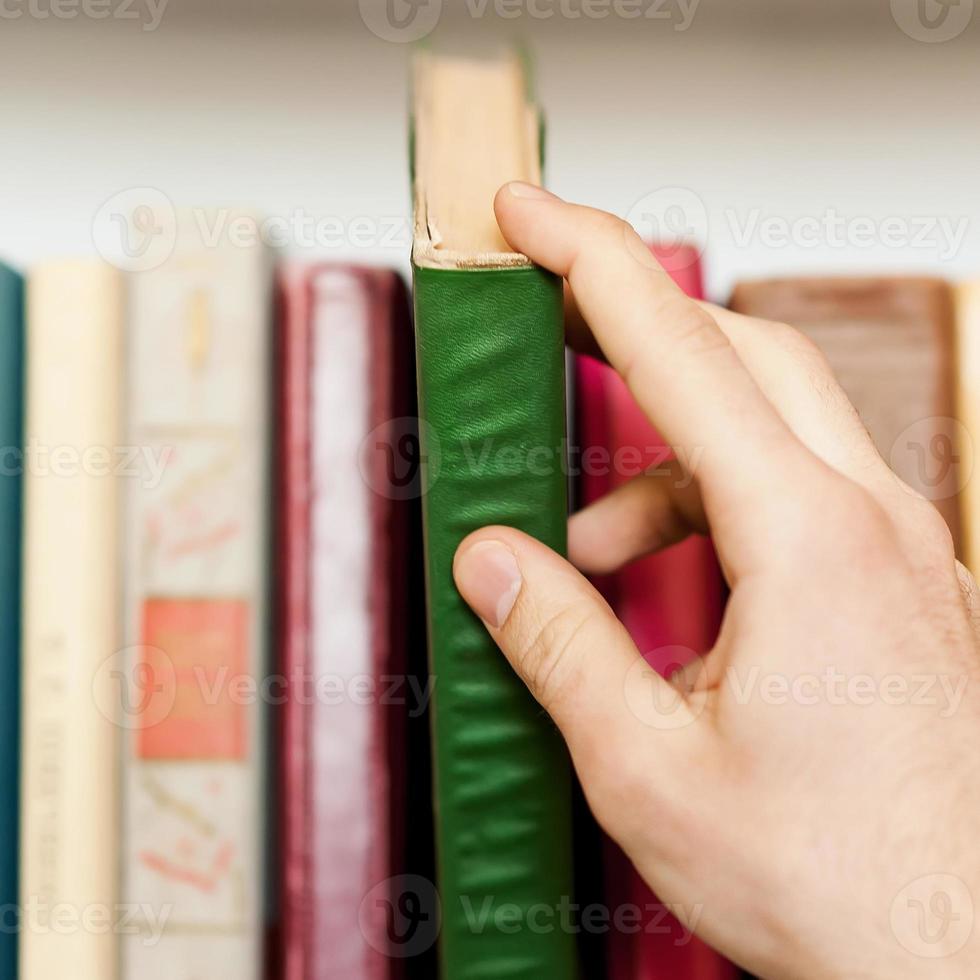 aqui está um livro que eu preciso. close-up de alguém pegando um livro da estante foto