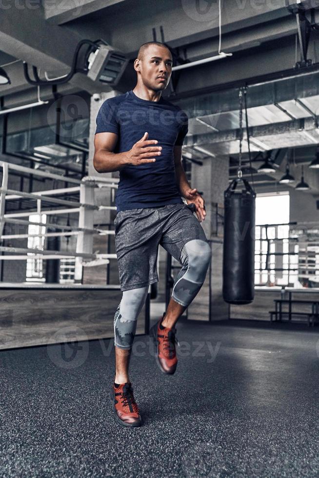 rumo ao estilo de vida mais saudável. comprimento total de jovem africano bonito em roupas esportivas pulando durante o exercício no ginásio foto