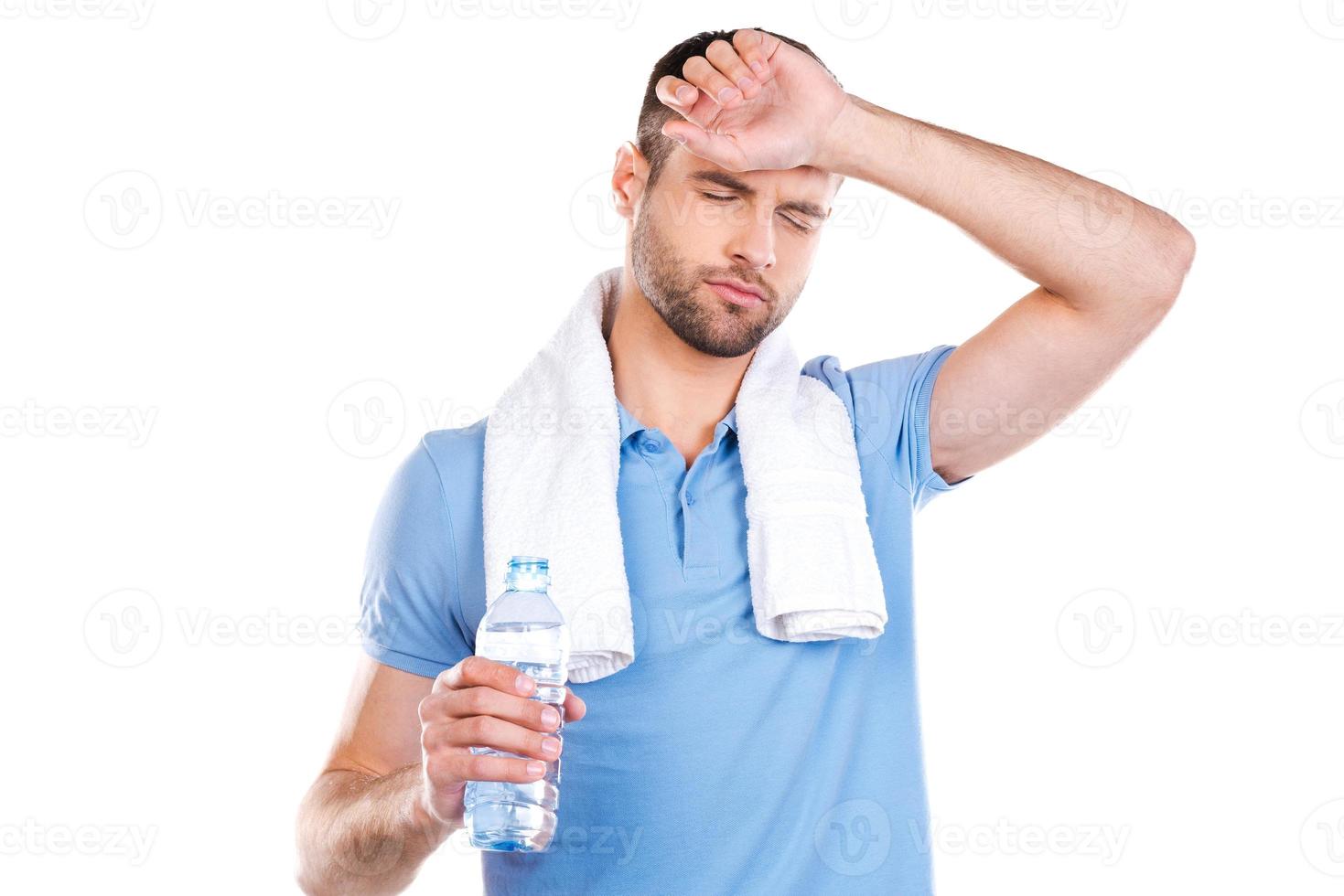 sentindo tão cansado. jovem cansado com toalha nos ombros, segurando a garrafa com água e sorrindo em pé contra um fundo branco foto