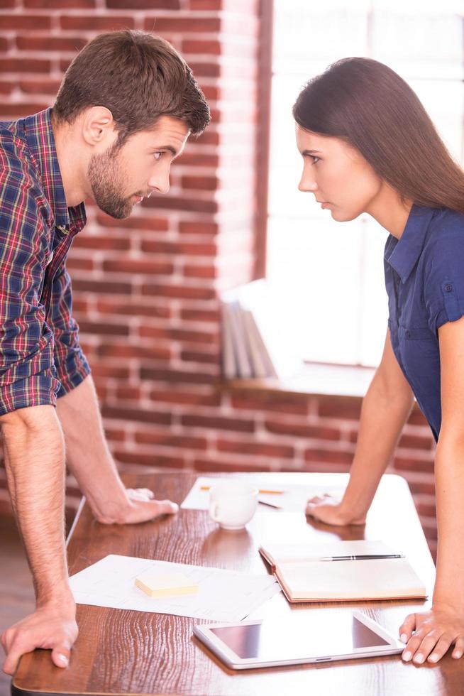 confronto empresarial. imagem de vista lateral de homem bravo e mulher em pé cara a cara enquanto se inclina na mesa do escritório foto