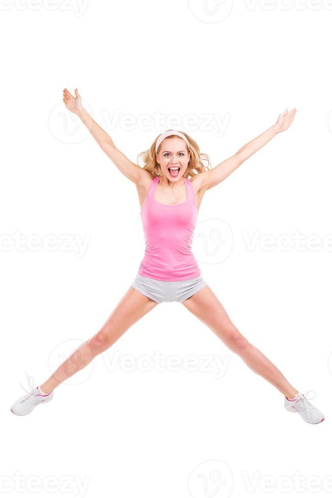 estrela loira. comprimento total da linda mulher de cabelos loiros em roupas esportivas rosa, mantendo os braços e as pernas esticadas enquanto pulava contra o fundo branco foto