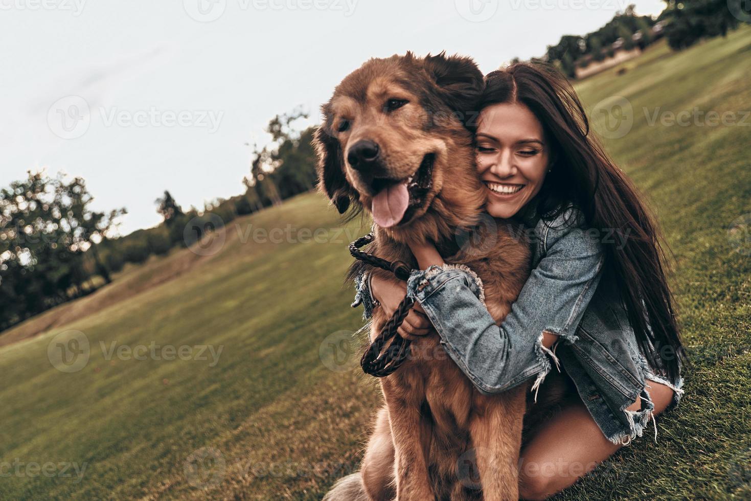 tão fofo e adorável. bela jovem mantendo os olhos fechados e sorrindo enquanto abraça seu cachorro ao ar livre foto