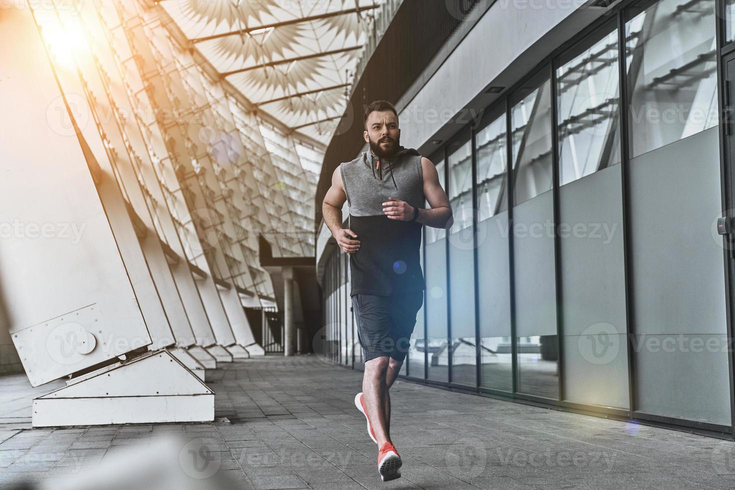 empurrando-se ao limite. comprimento total de jovem bonito em roupas esportivas, olhando para longe enquanto corre lá fora foto