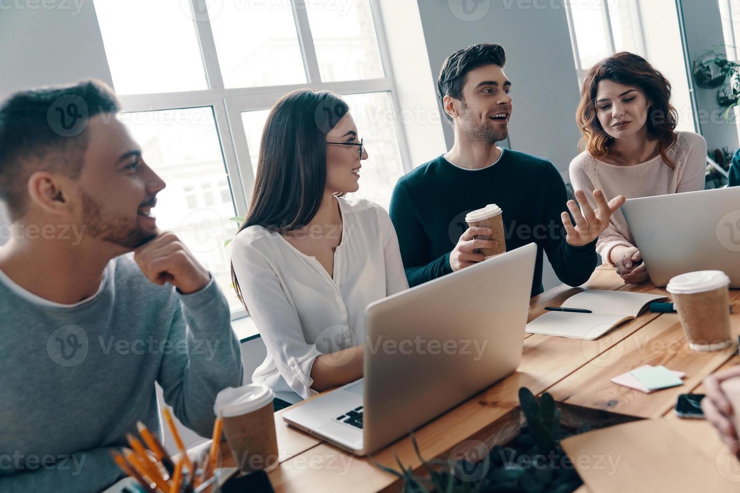 parceiros de negócios felizes. grupo de jovens modernos em roupas casuais inteligentes discutindo algo e sorrindo enquanto trabalhava no escritório criativo foto