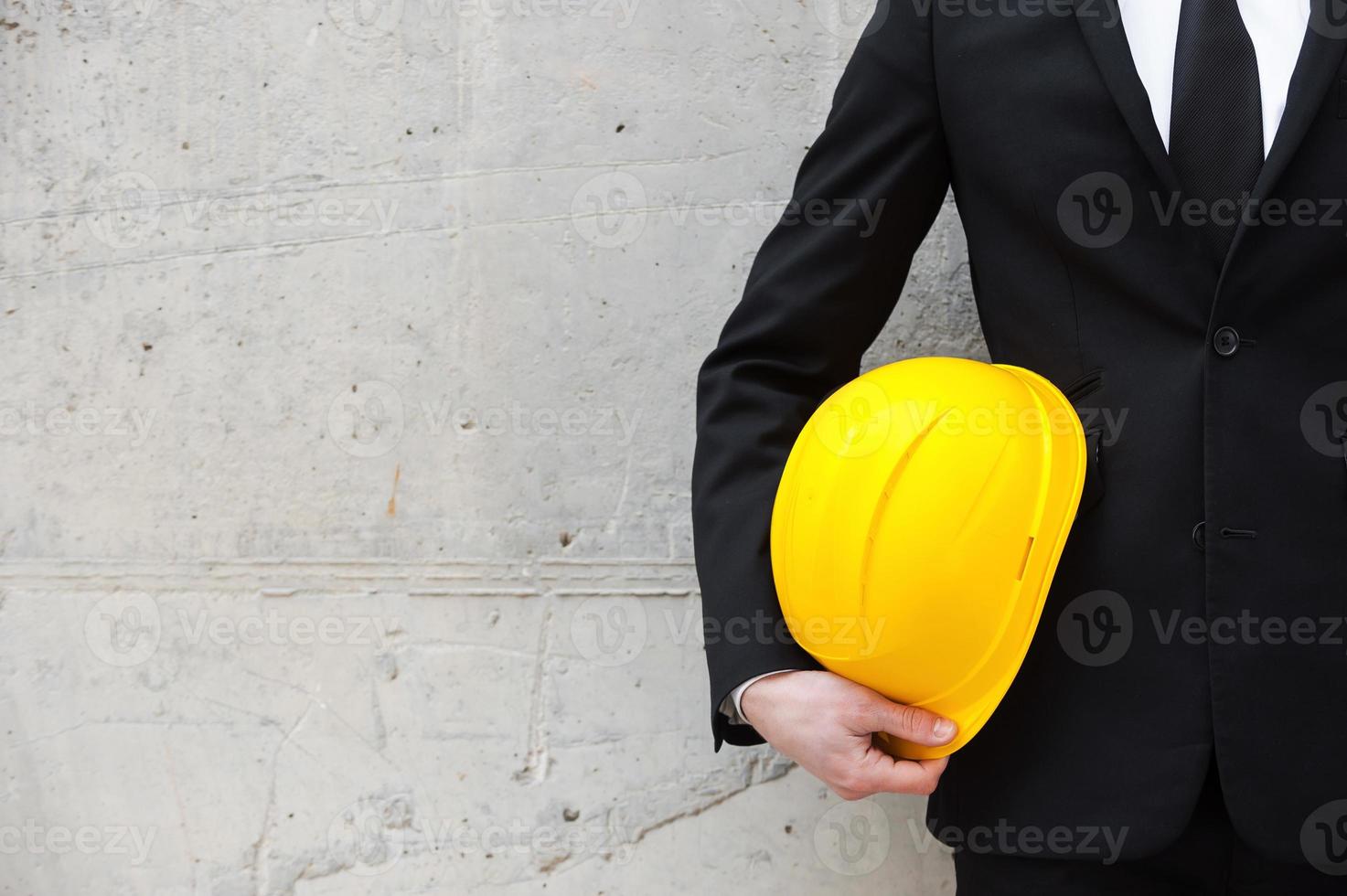 pronto para novo projeto. imagem recortada de homem em traje formal, segurando o capacete em pé contra a parede de concreto foto