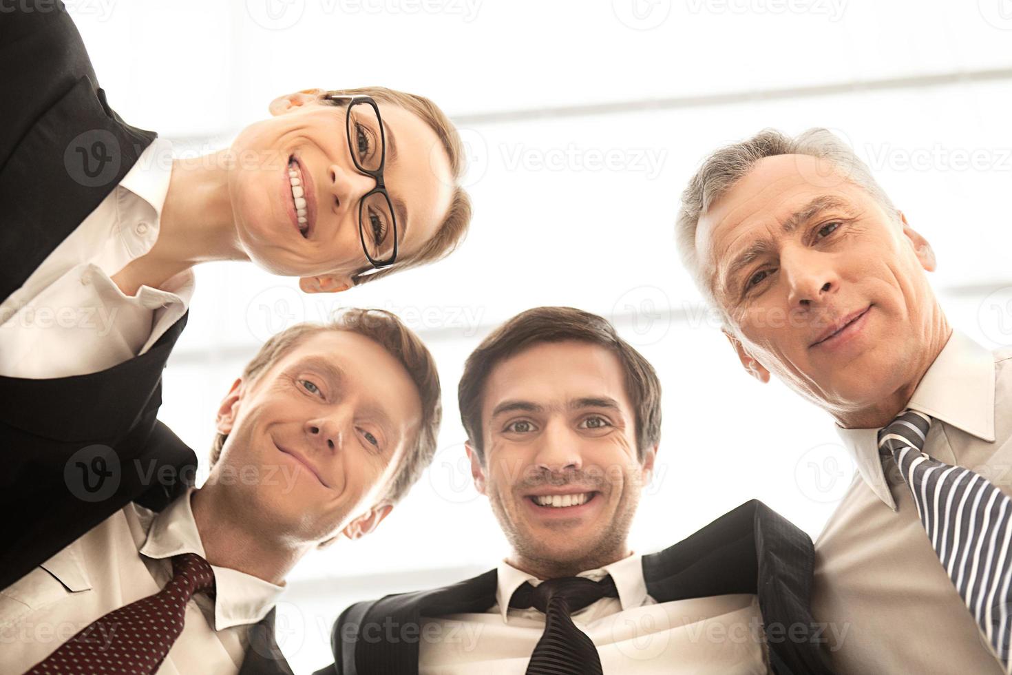 somos uma equipe de negócios forte. vista de ângulo baixo de quatro empresários alegres em pé perto um do outro e sorrindo para a câmera foto
