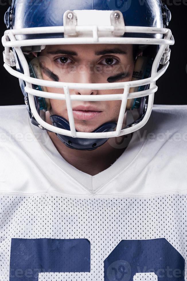 guerreiro destemido. retrato de jogador de futebol americano olhando para a câmera em pé contra um fundo preto foto