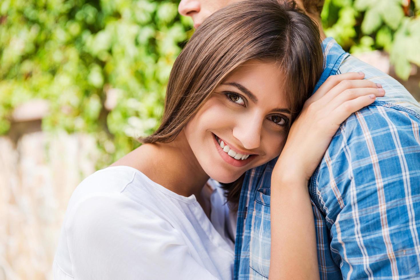 sentindo-se seguro e tranquilo. mulher jovem e bonita se ligando ao namorado e sorrindo para a câmera enquanto ambos estão ao ar livre foto