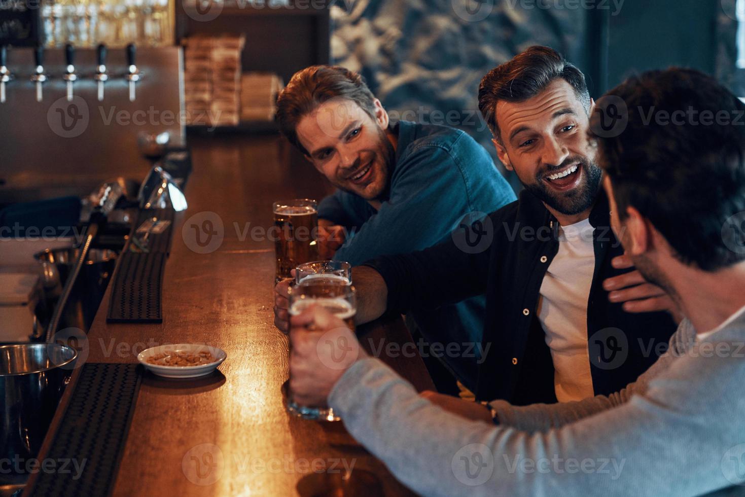 jovens despreocupados em roupas casuais bebendo cerveja e se unindo enquanto estão sentados no pub foto