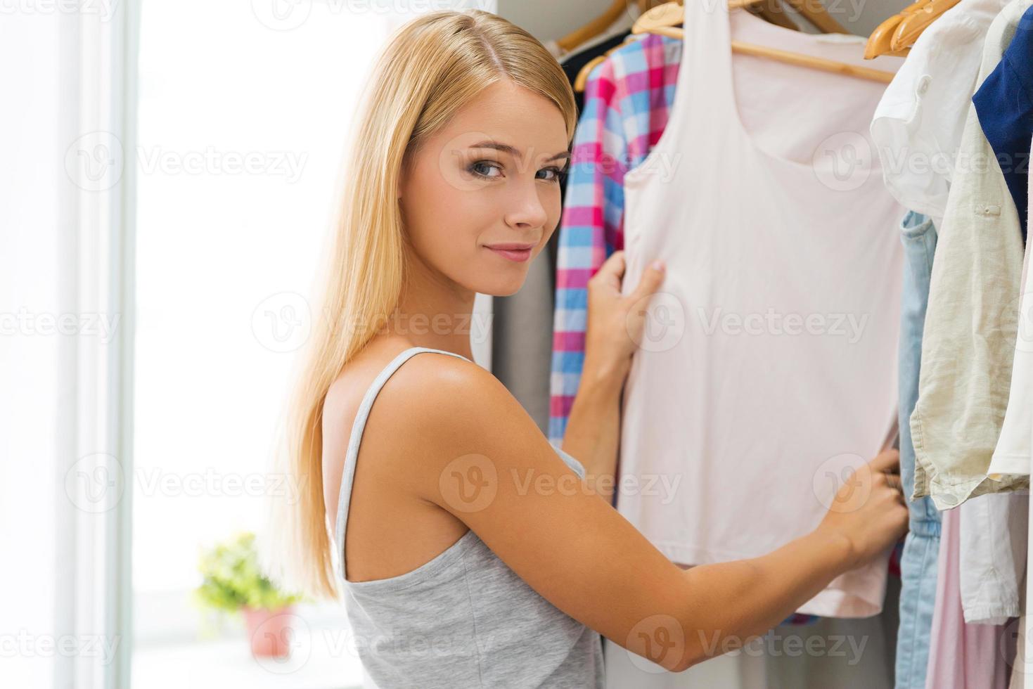 escolhendo roupa para hoje. jovem sorridente escolhendo roupas e olhando para a câmera em pé perto de seu guarda-roupa foto