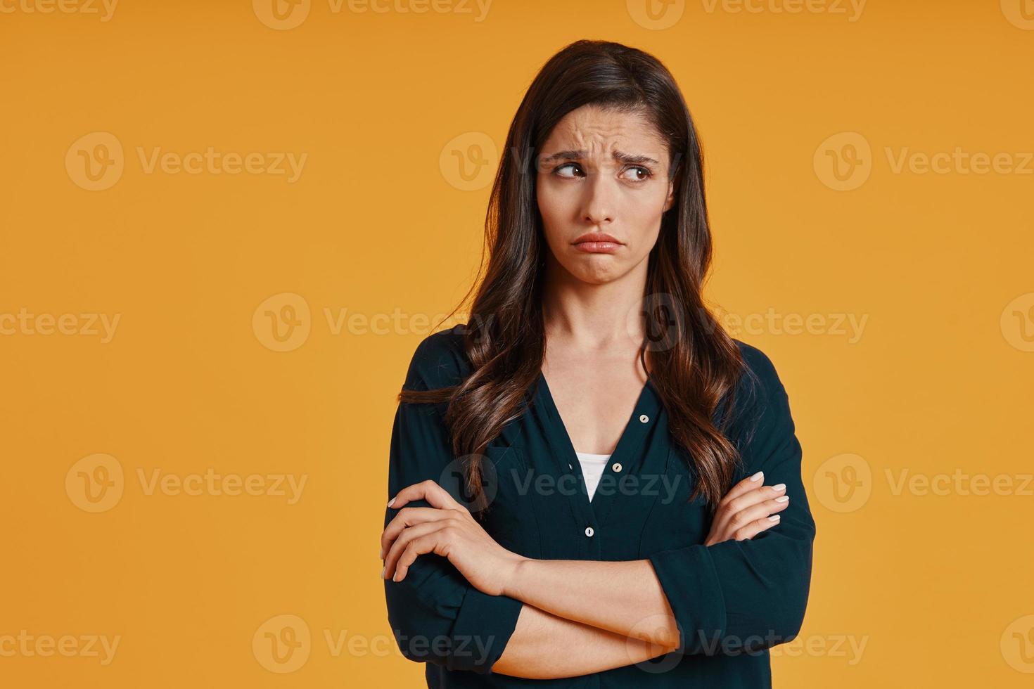 jovem triste em roupas casuais, fazendo uma careta em pé contra um fundo amarelo foto