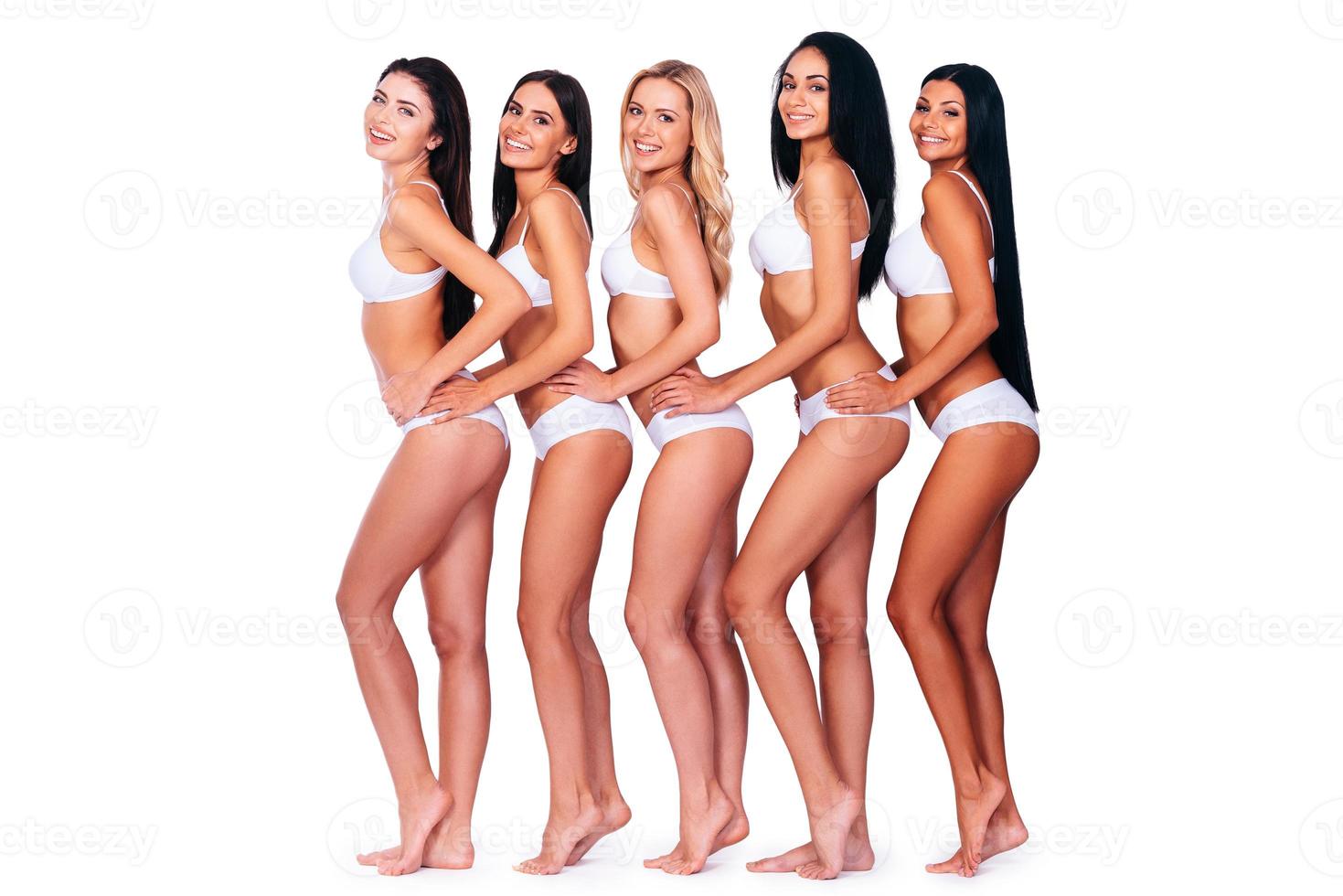 belezas em linha. vista lateral de corpo inteiro de cinco mulheres bonitas em lingerie olhando para a câmera e sorrindo em pé contra um fundo branco foto