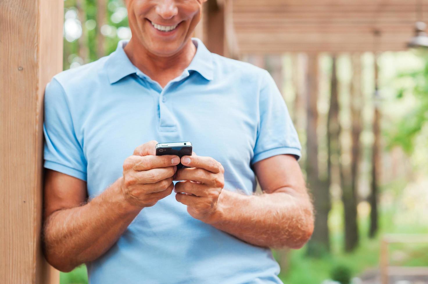 examinando seu novo telefone inteligente. alegre homem maduro segurando o celular e sorrindo em pé ao ar livre foto
