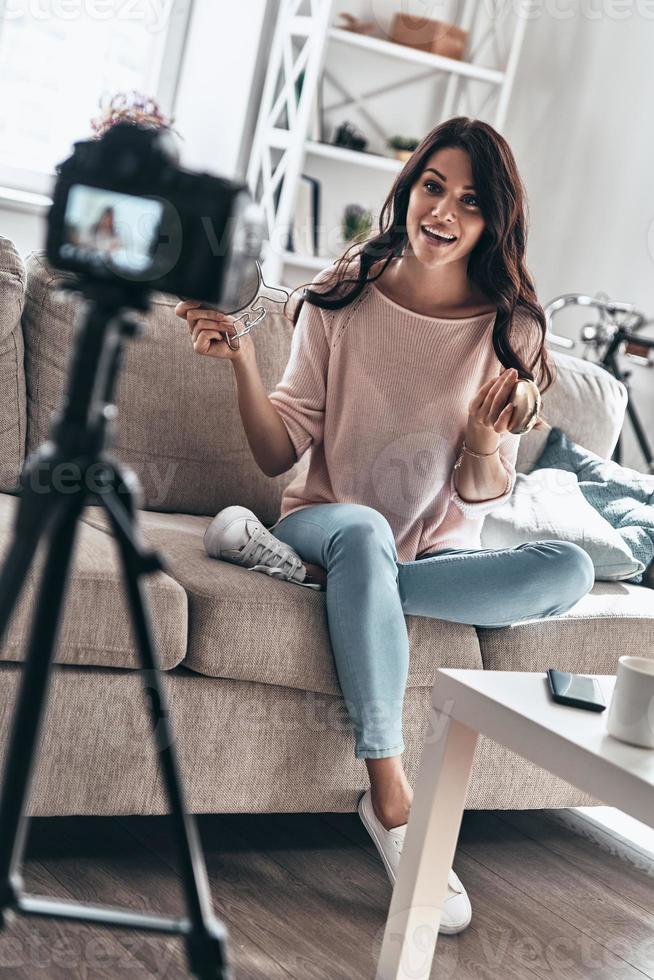 vlogger moderno. bela jovem segurando produtos de beleza e sorrindo enquanto faz vídeo de mídia social foto