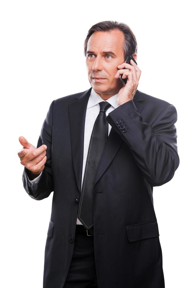 conversa séria de negócios. homem maduro sério de camisa e gravata falando no celular e gesticulando em pé isolado no fundo branco foto