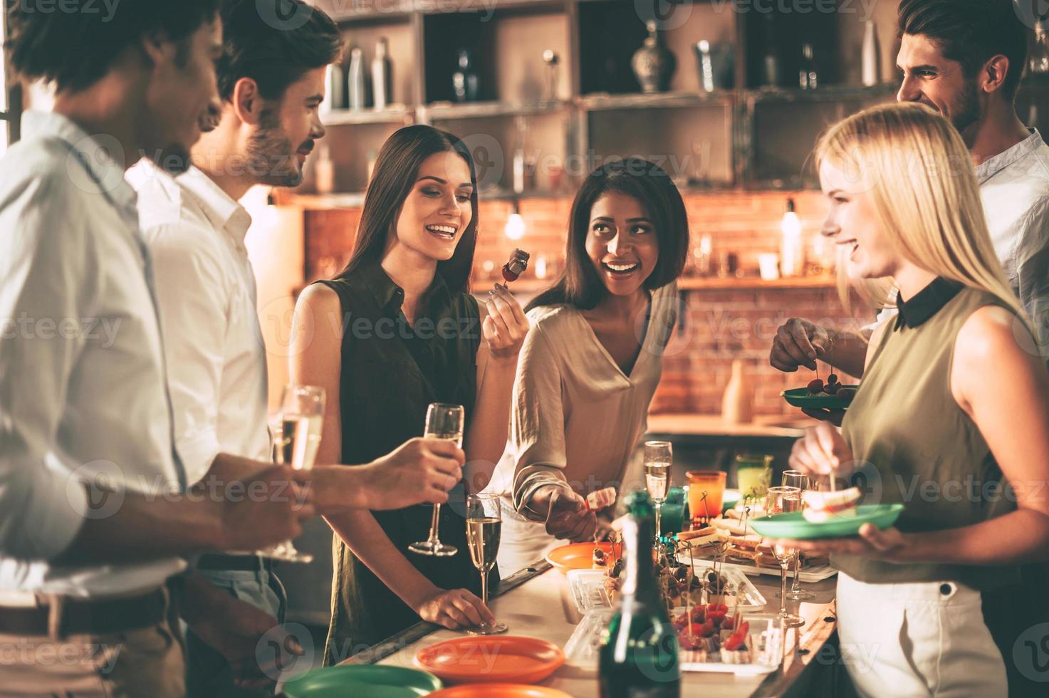 curtindo a festa em casa. grupo de jovens alegres curtindo a festa em casa com lanches e bebidas enquanto se comunicam na cozinha foto