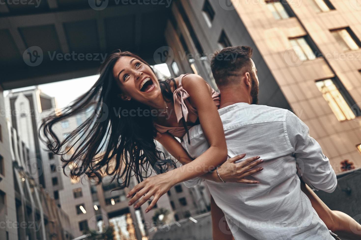 sentindo brincalhão. bela jovem mantendo a boca aberta enquanto o namorado a carregando ao ar livre foto