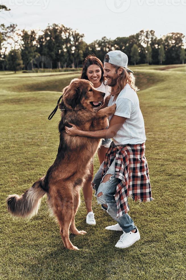 comprimento total do jovem casal moderno brincando com seu cachorro em pé no parque foto