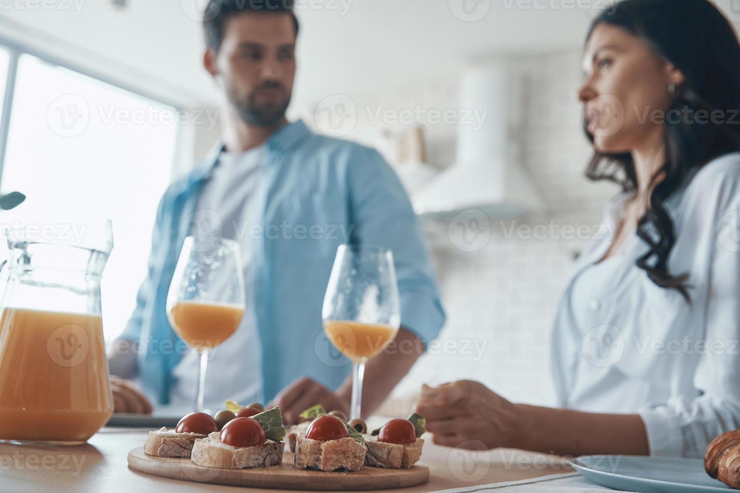 lindo casal jovem conversando e preparando o café da manhã enquanto passa o tempo na cozinha doméstica foto