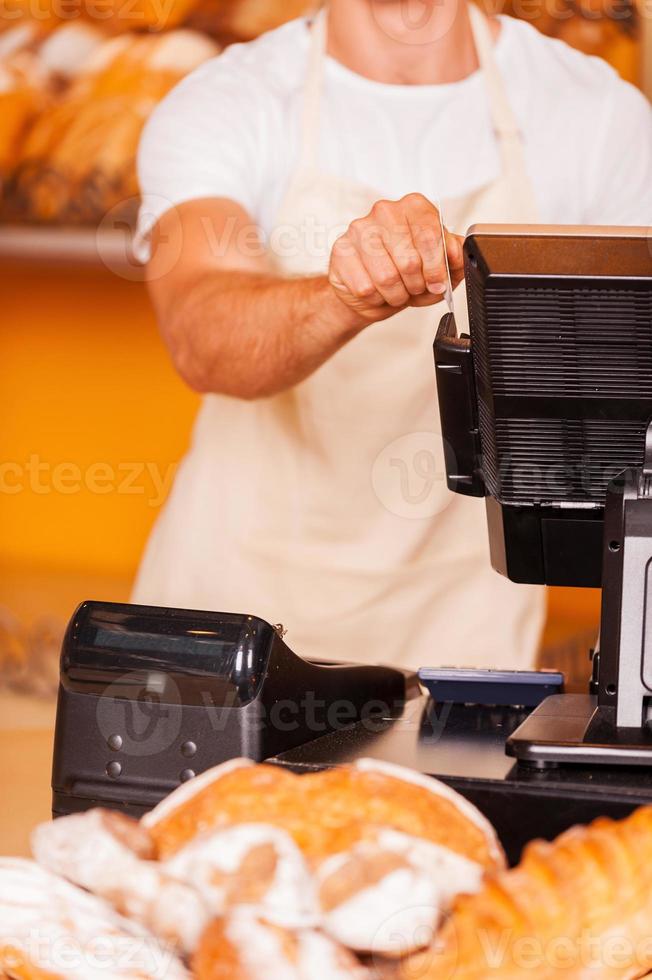 caixa no trabalho. close-up do caixa masculino passa um cartão de plástico através de uma máquina em pé na padaria foto