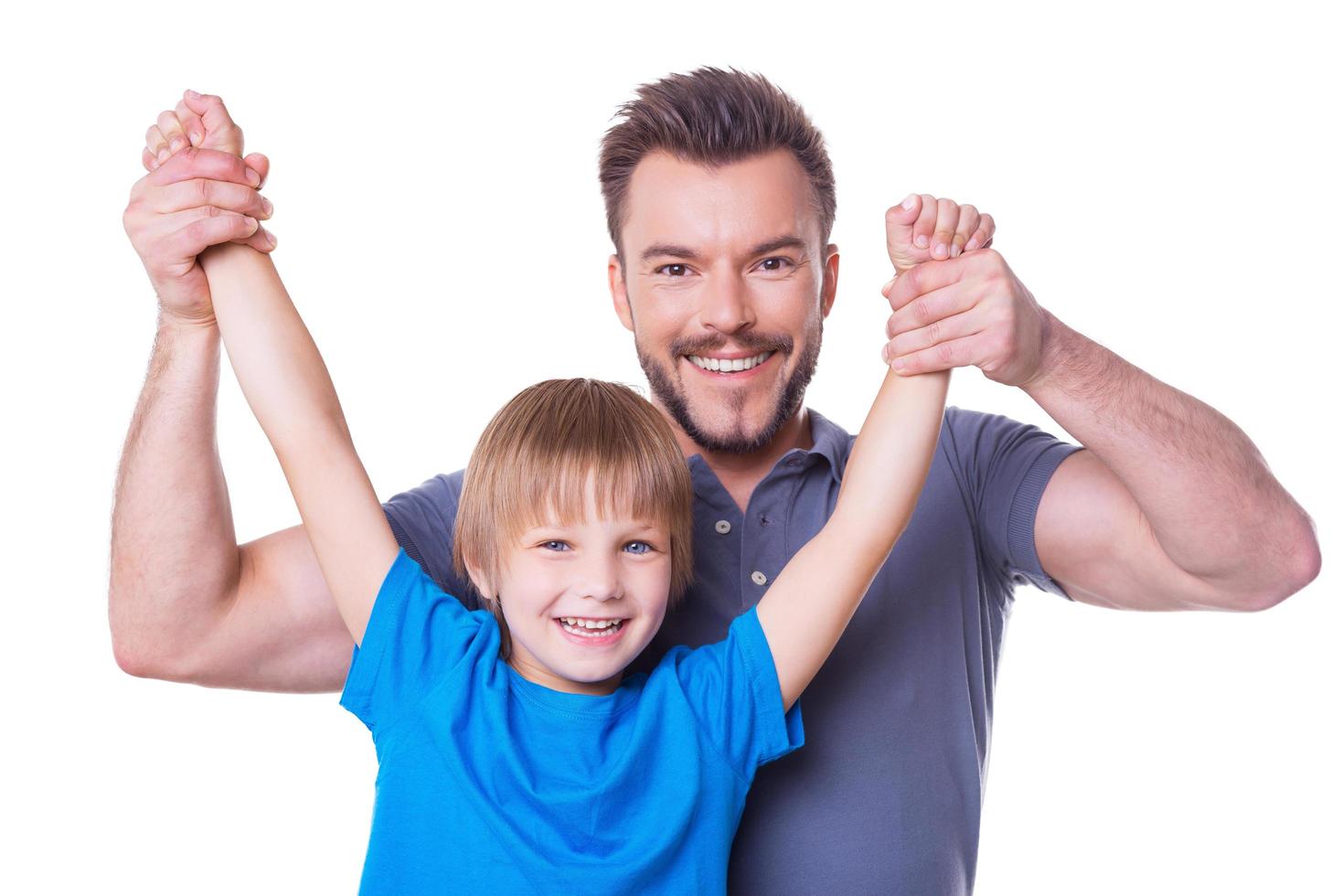 se divertindo juntos. pai feliz carregando seu filho brincalhão pelas mãos e sorrindo enquanto ambos estão isolados no branco foto