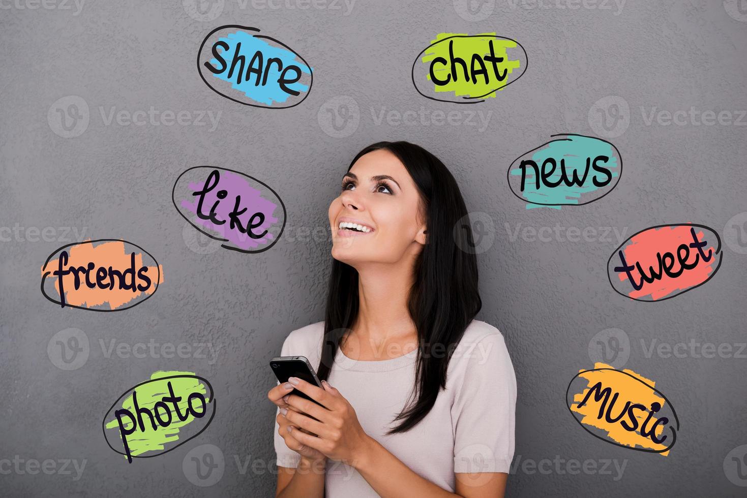 aproveitando as novas tecnologias. mulher jovem feliz segurando o telefone inteligente e olhando para esboços coloridos na cabeça foto