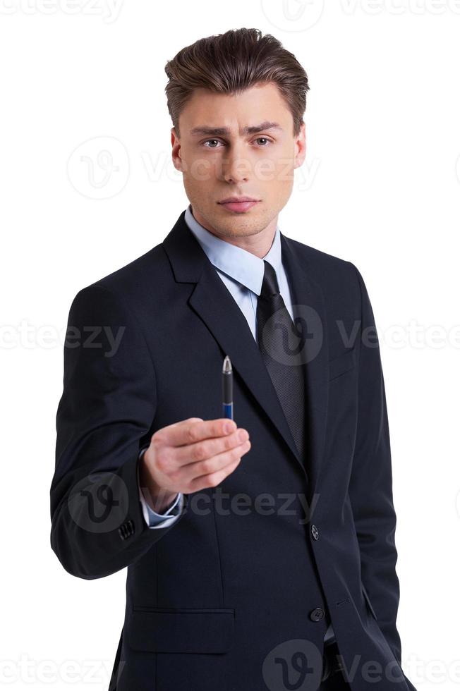 assine o retrato do contrato de um jovem confiante em trajes formais esticando a caneta e olhando para a câmera em pé isolado no branco foto