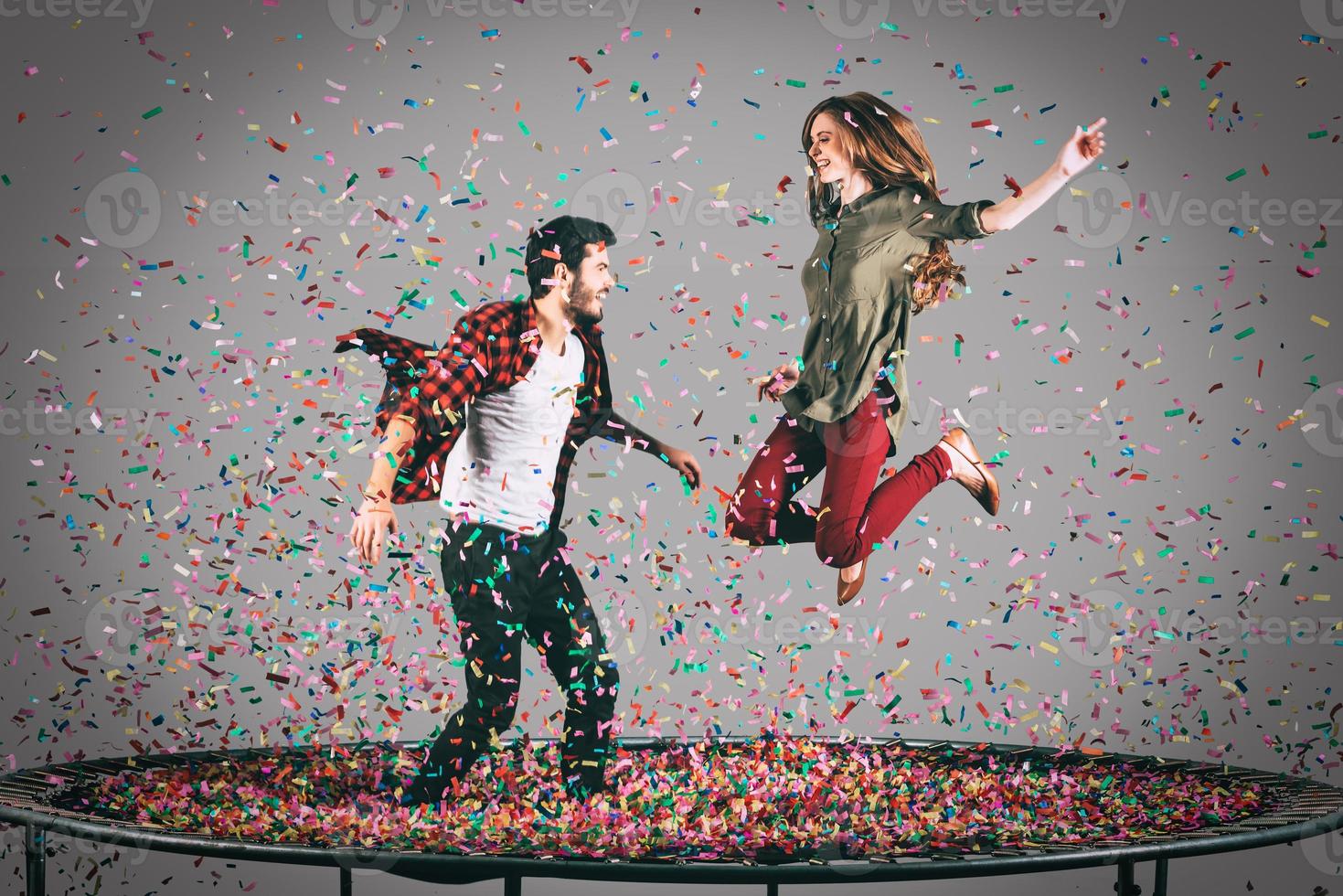 apenas por diversão. tiro no ar do belo casal alegre pulando no trampolim junto com confete ao redor deles foto