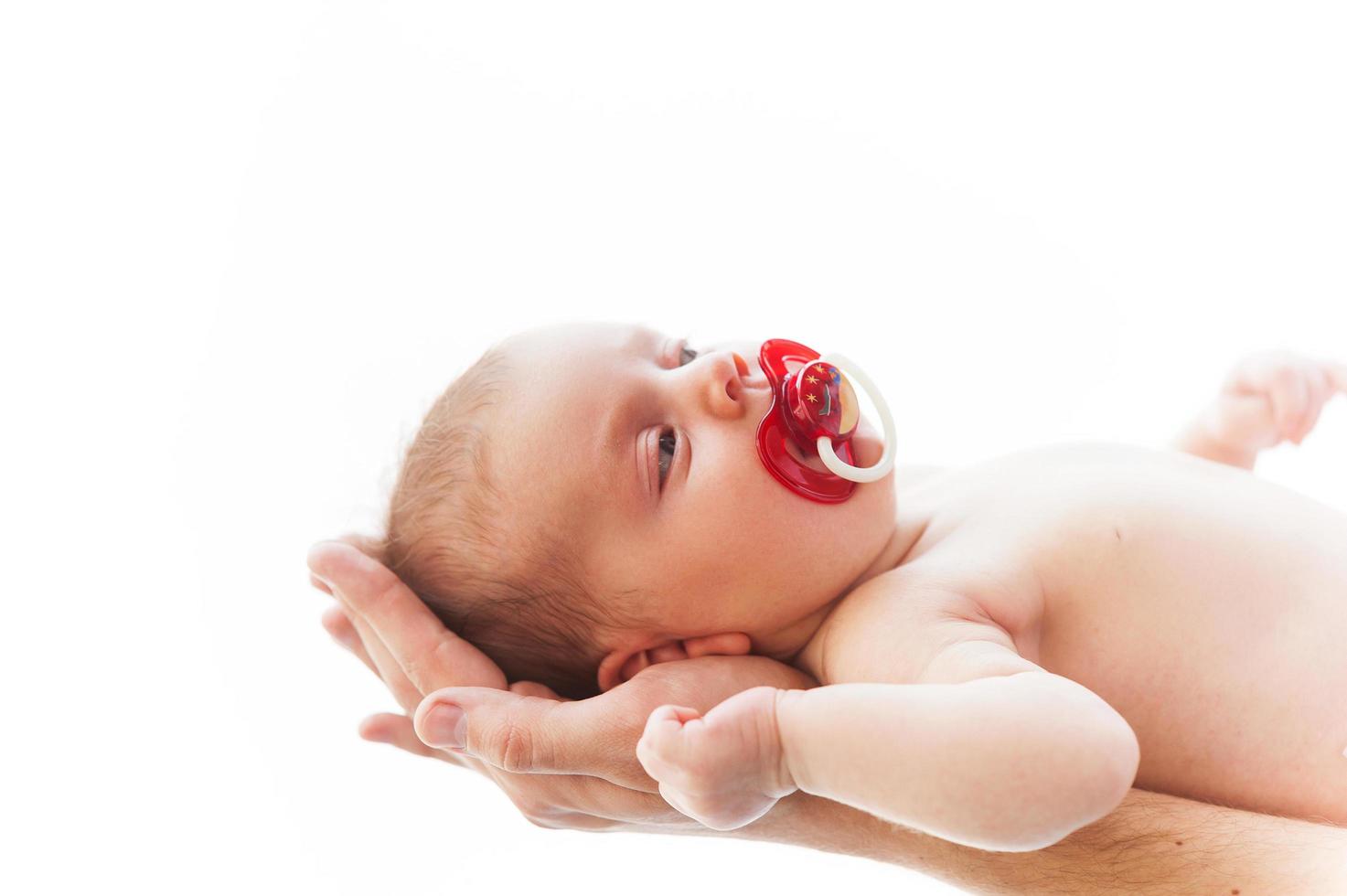 pequeno bebê. close-up de mãos masculinas segurando um bebezinho com chupeta na boca foto