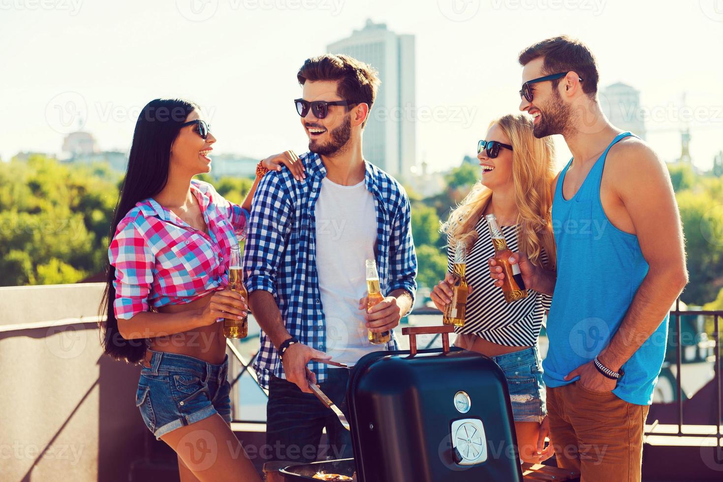 momentos alegres com os amigos. grupo de jovens alegres segurando garrafas com cerveja e churrasco em pé no telhado foto