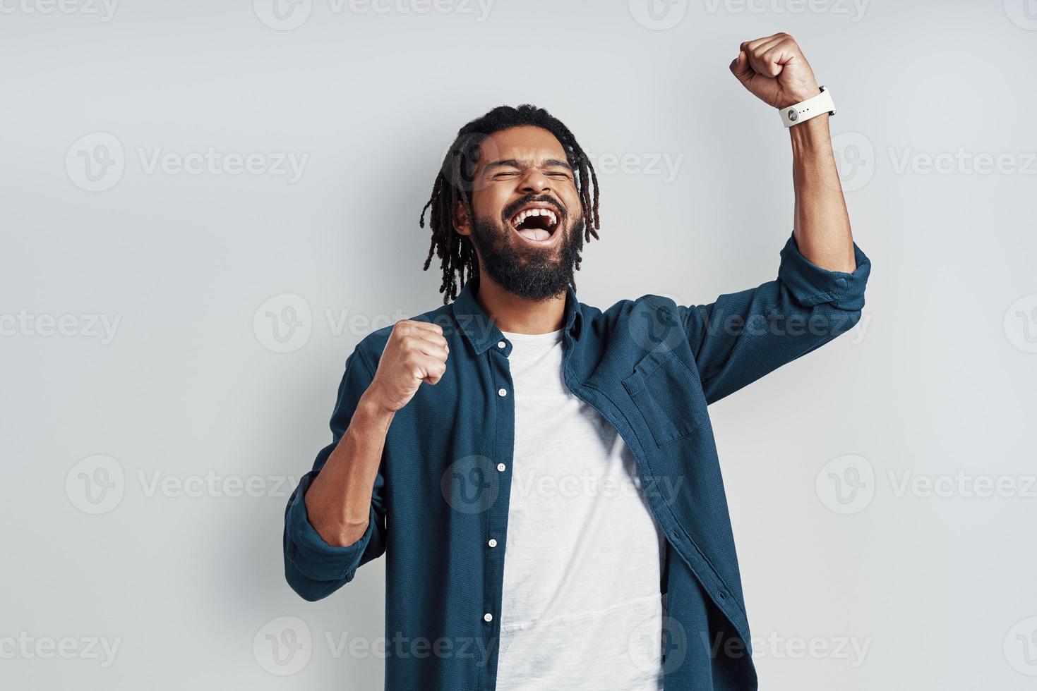 alegre jovem africano em roupas casuais, gritando e gesticulando em pé contra um fundo cinza foto