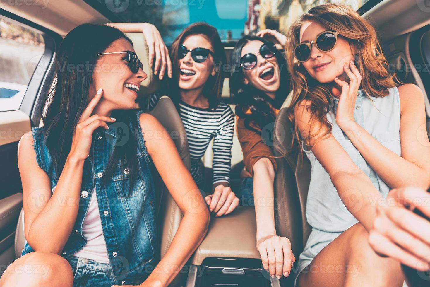 curtindo a viagem juntos. quatro belas jovens alegres olhando feliz e brincalhão enquanto está sentado no carro foto