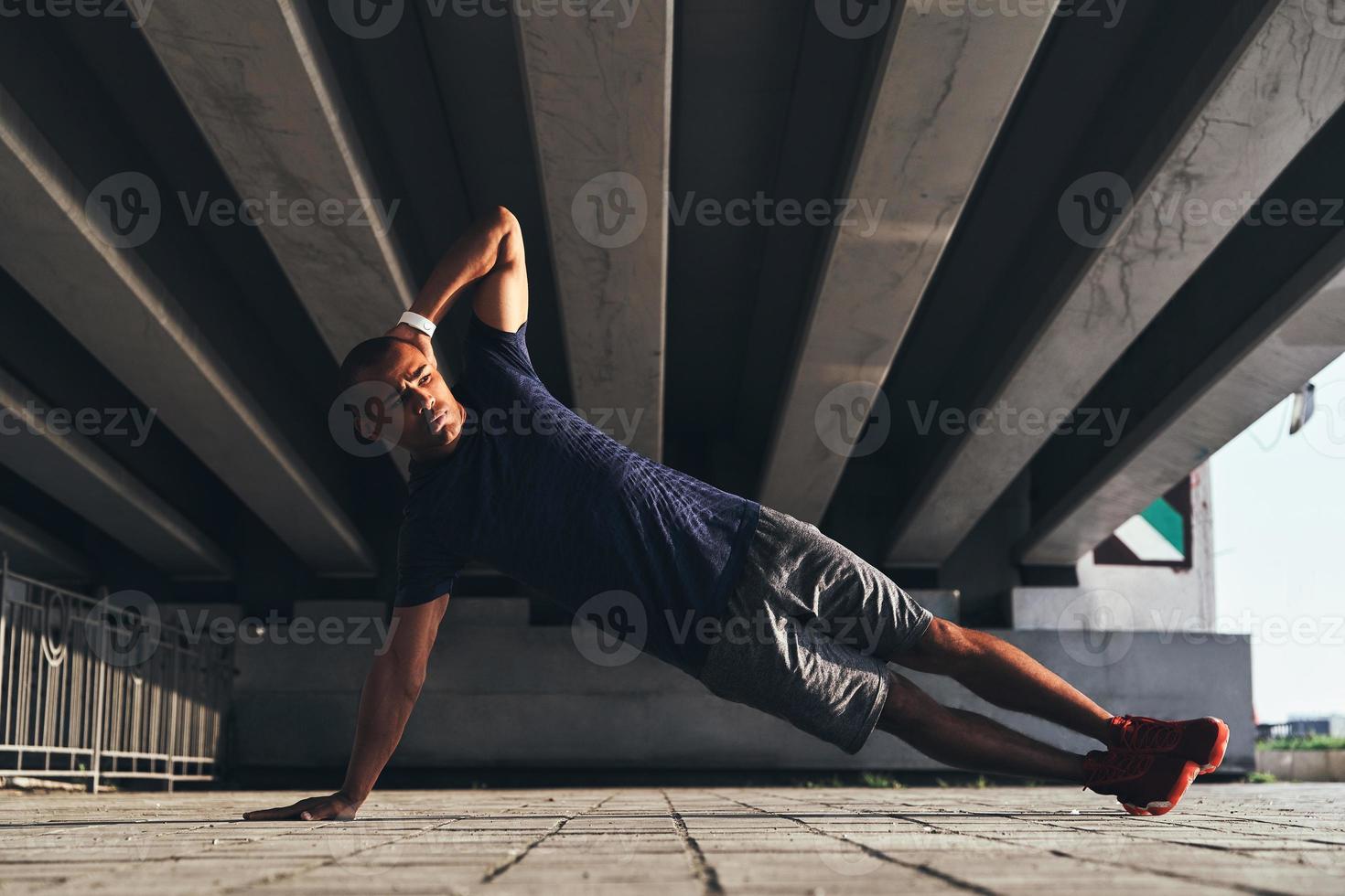 treinando para ser o melhor. jovem africano bonito em roupas esportivas, mantendo a posição de prancha enquanto se exercita ao ar livre foto