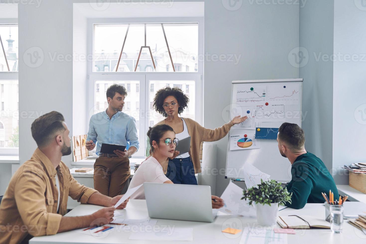 grupo de jovens confiantes em roupas casuais inteligentes discutindo negócios enquanto se reúnem no escritório foto