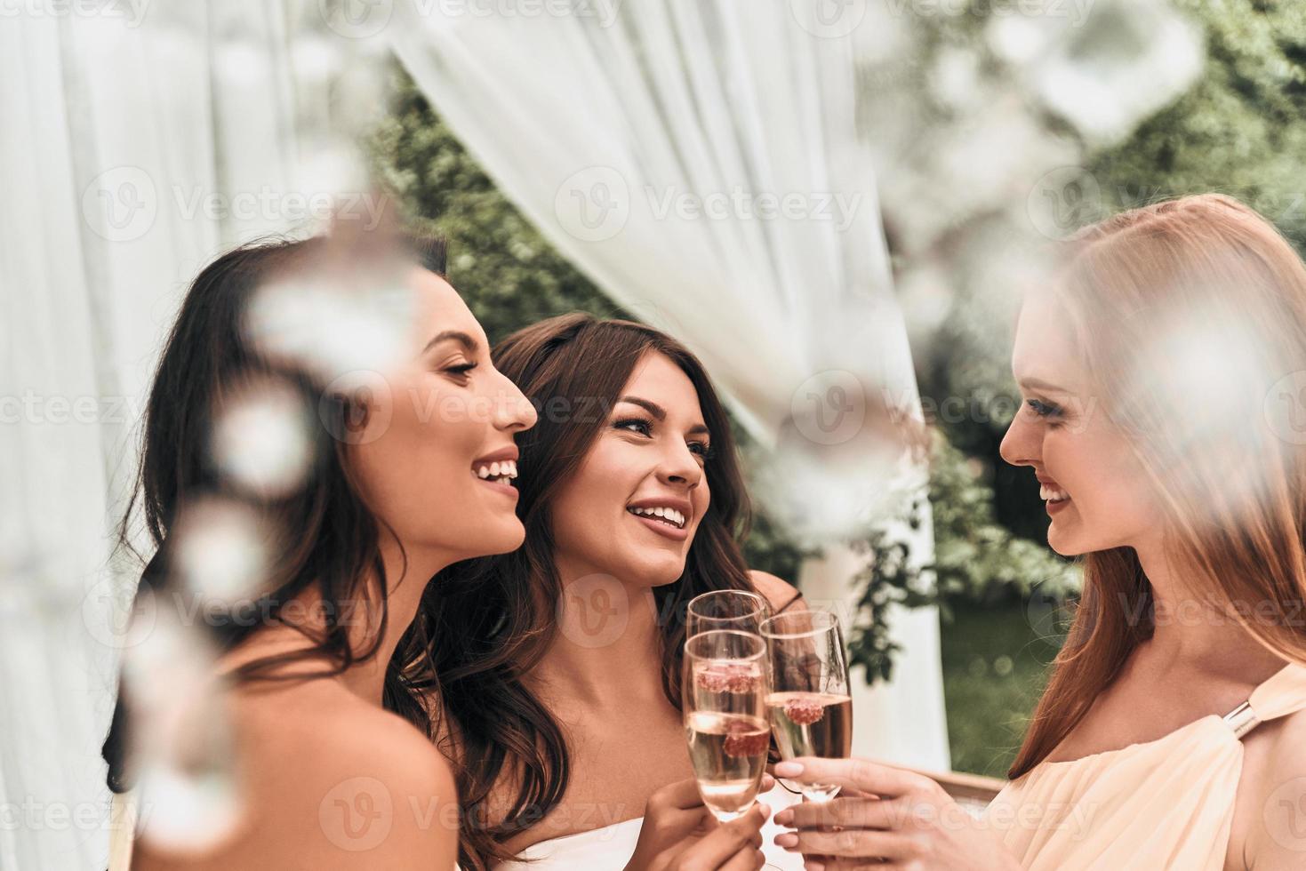 melhores amigos estão sempre por perto. atraente jovem noiva brindando com champanhe com suas belas damas de honra em pé ao ar livre juntos foto