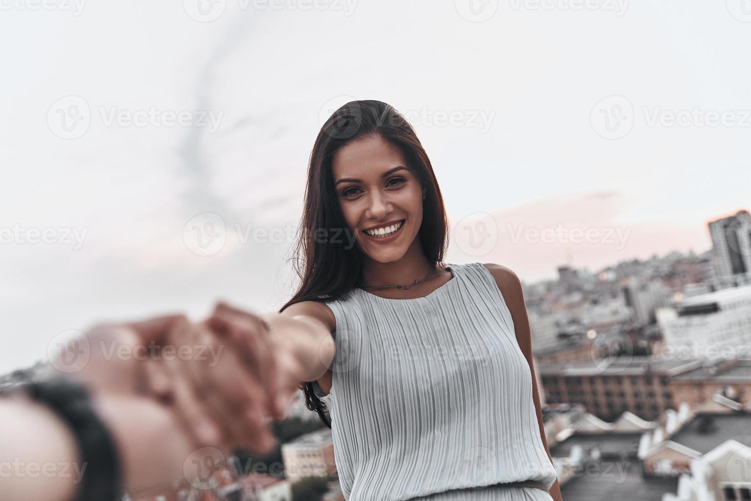 bela jovem sorrindo e olhando para a câmera enquanto de mãos dadas com o namorado ao ar livre foto