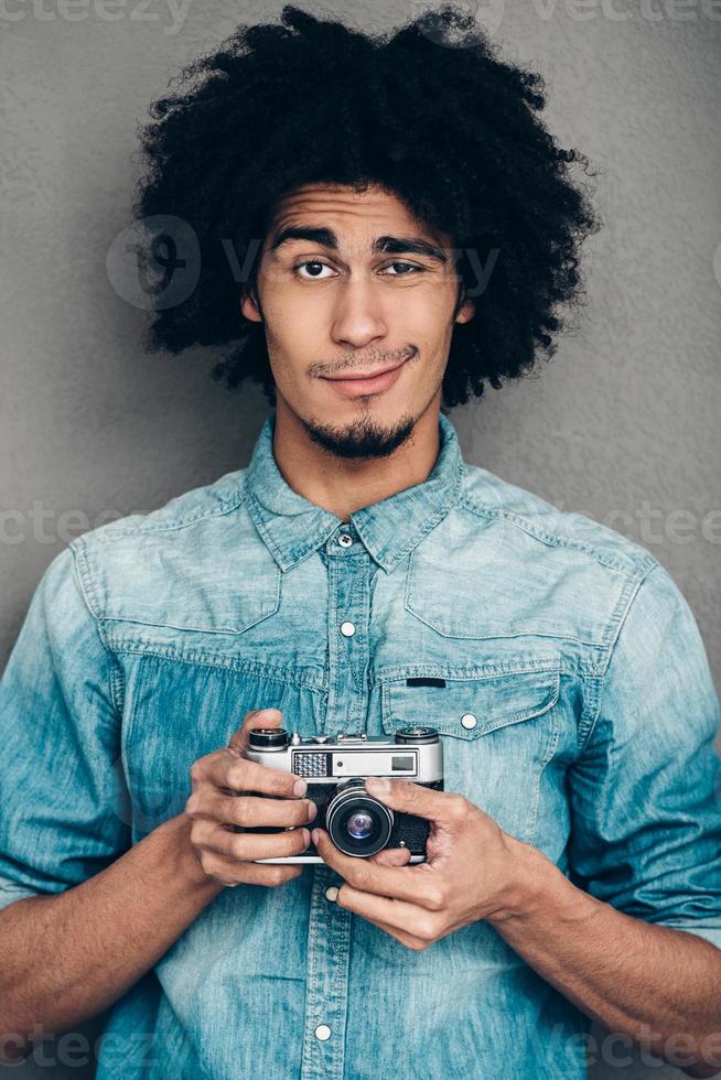 precisamos mudar sua pose jovem africano segurando a câmera com estilo retrô e olhando para a câmera em pé contra um fundo cinza foto