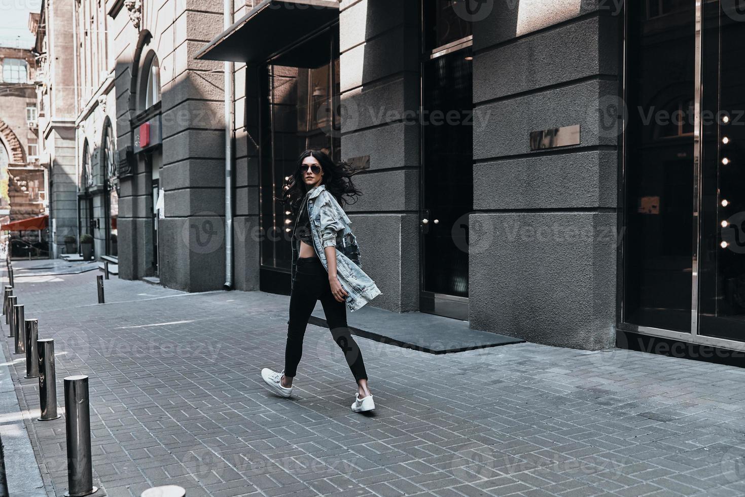 garota da cidade. vista traseira de corpo inteiro de jovem olhando por cima do ombro enquanto caminhava pela rua foto