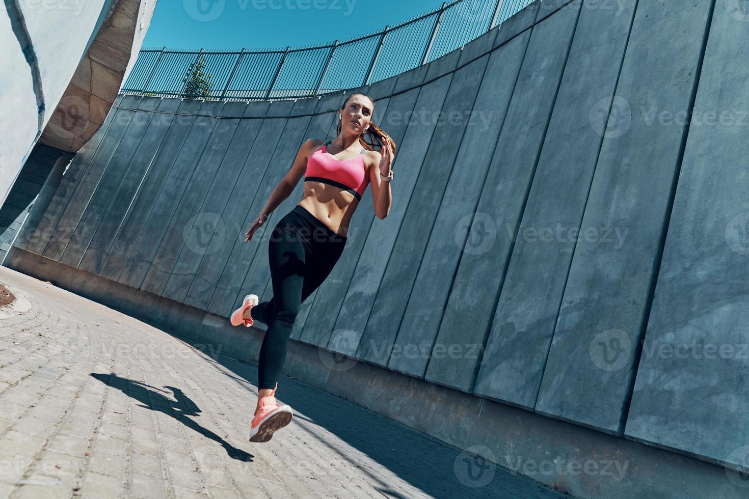 comprimento total de mulher jovem e bonita em roupas esportivas correndo ao ar livre foto