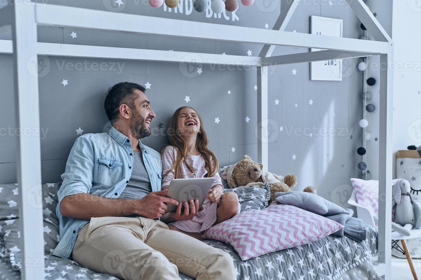 desenhos engraçados online. jovem pai e sua filha usando tablet digital enquanto está sentado na cama em casa foto