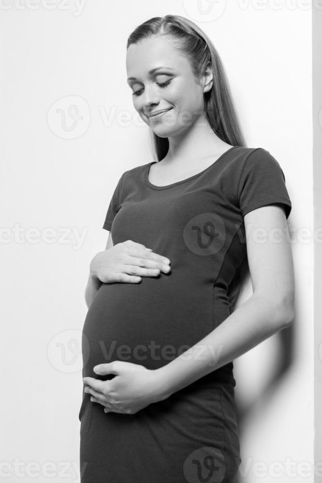 mulher grávida. imagem em preto e branco da bela jovem grávida tocando seu abdômen e olhando para ele com um sorriso foto